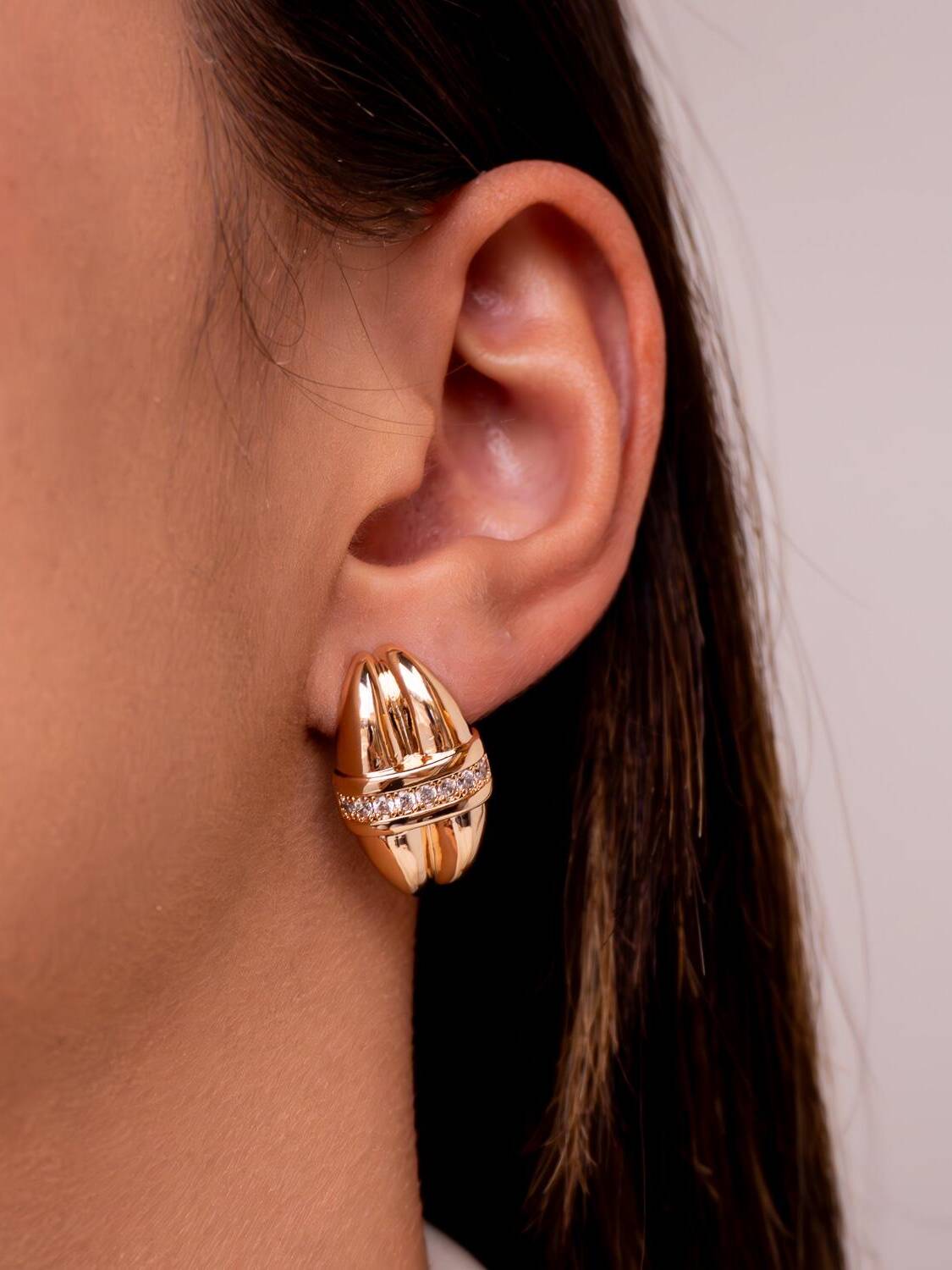Boucle d’oreille dorée bombée à deux rangées côtelées séparées par une bande de pierres claires.