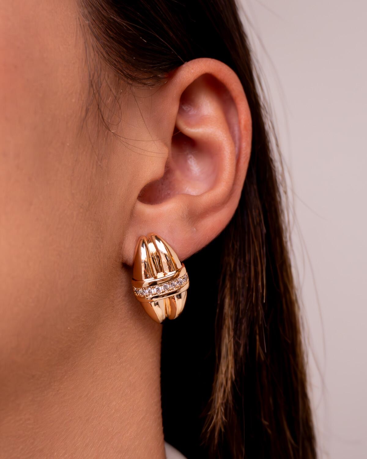 Boucle d’oreille dorée bombée à deux rangées côtelées séparées par une bande de pierres claires.
