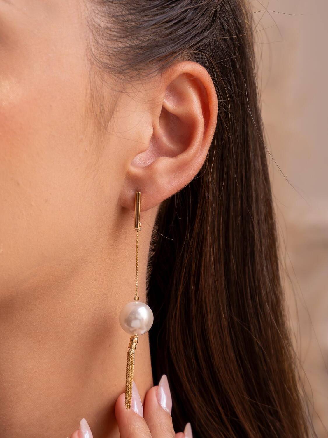 Boucle d’oreille longue dorée : barre, chaîne fine, grosse perle ronde et frange de métal.