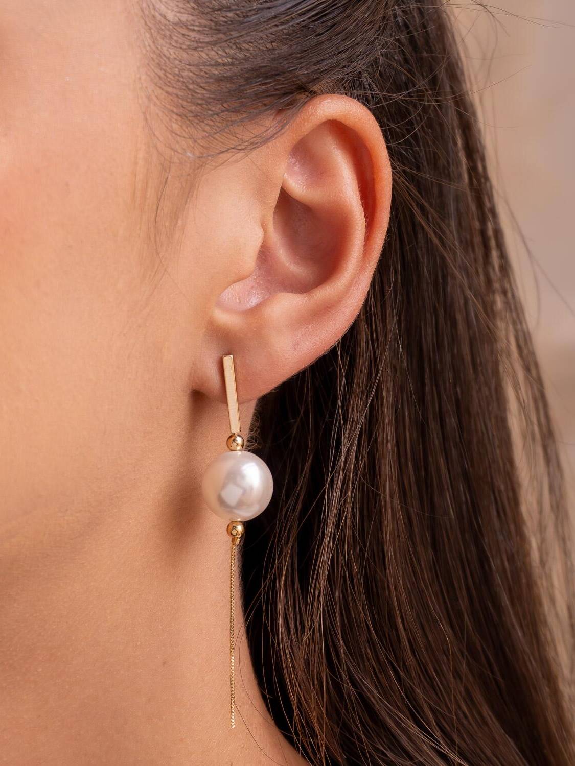 Boucle d’oreille dorée : barre, petites billes, perle ronde centrale et fine chaîne pendante.