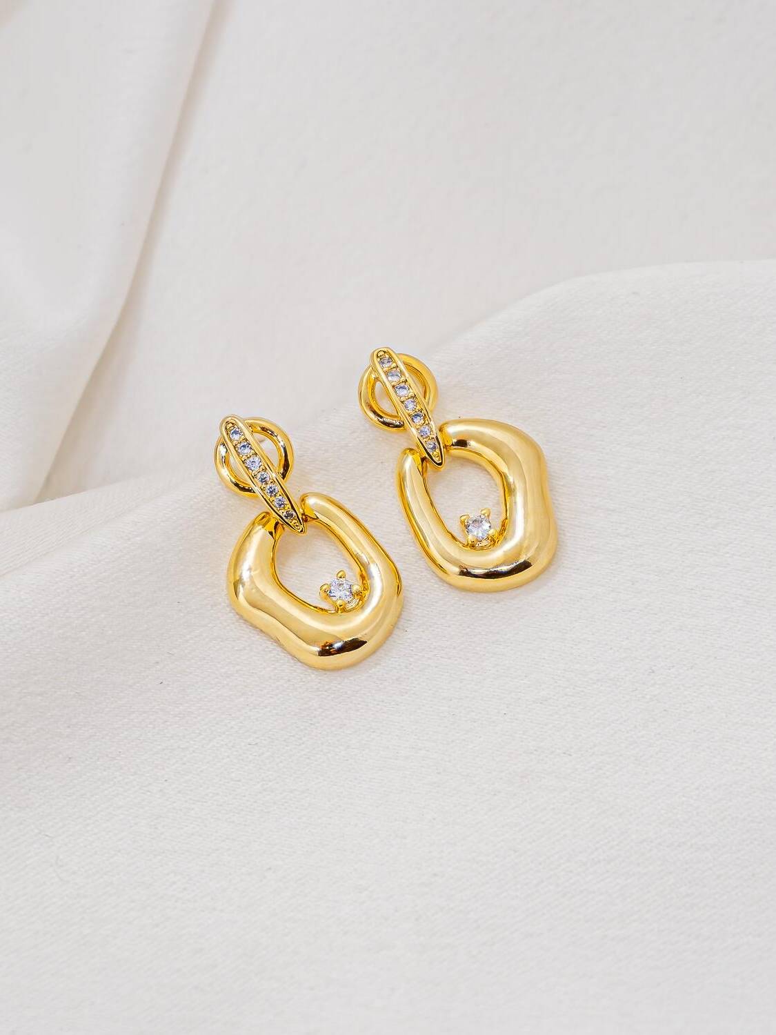 Boucles d’oreilles dorées, barrette sertie de pierres claires et pendentif ovale lisse avec pierre centrale