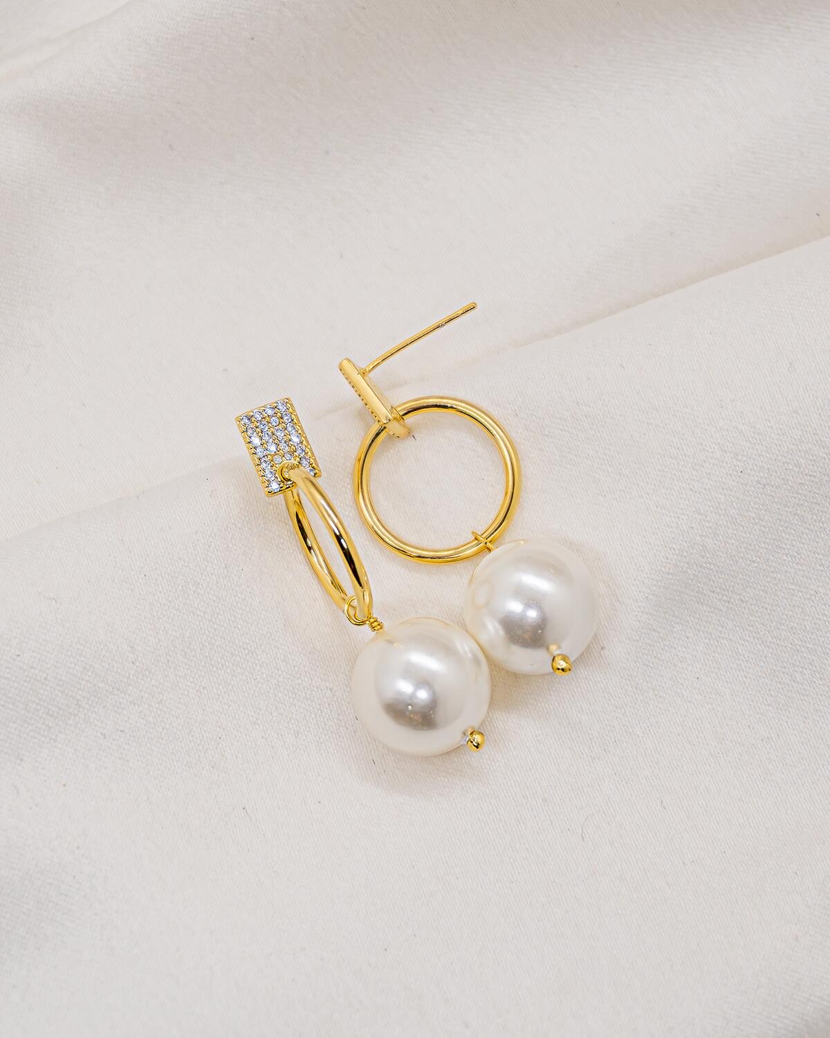 Paire de boucles d’oreilles dorées : anneau lisse, base de pierres claires et grosse perle blanche.