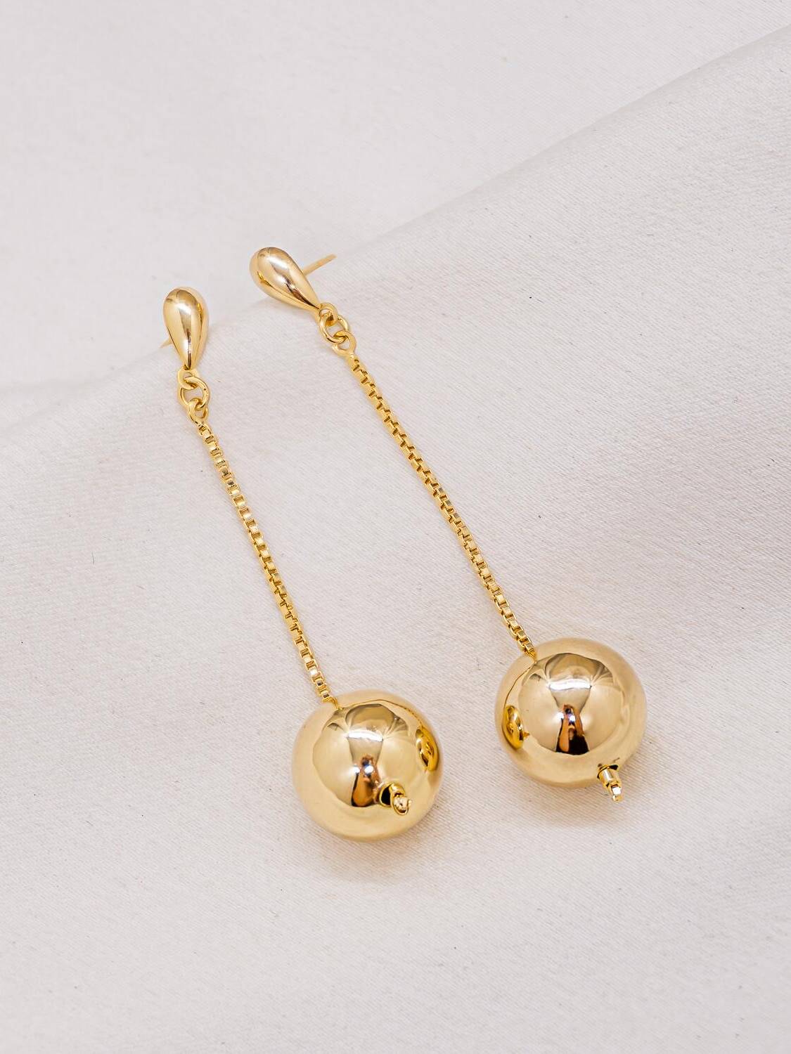 Paire de boucles d’oreilles dorées pendantes avec chaîne fine et grosse boule brillante