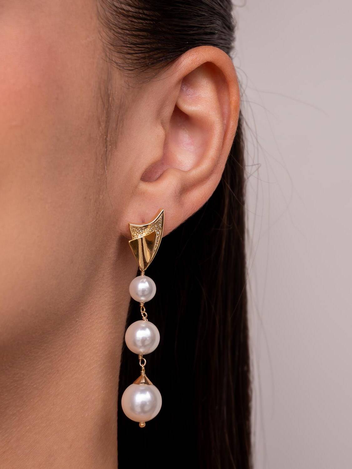 Boucle d’oreille longue : base dorée organique texturée et trois perles blanches rondes en cascade.