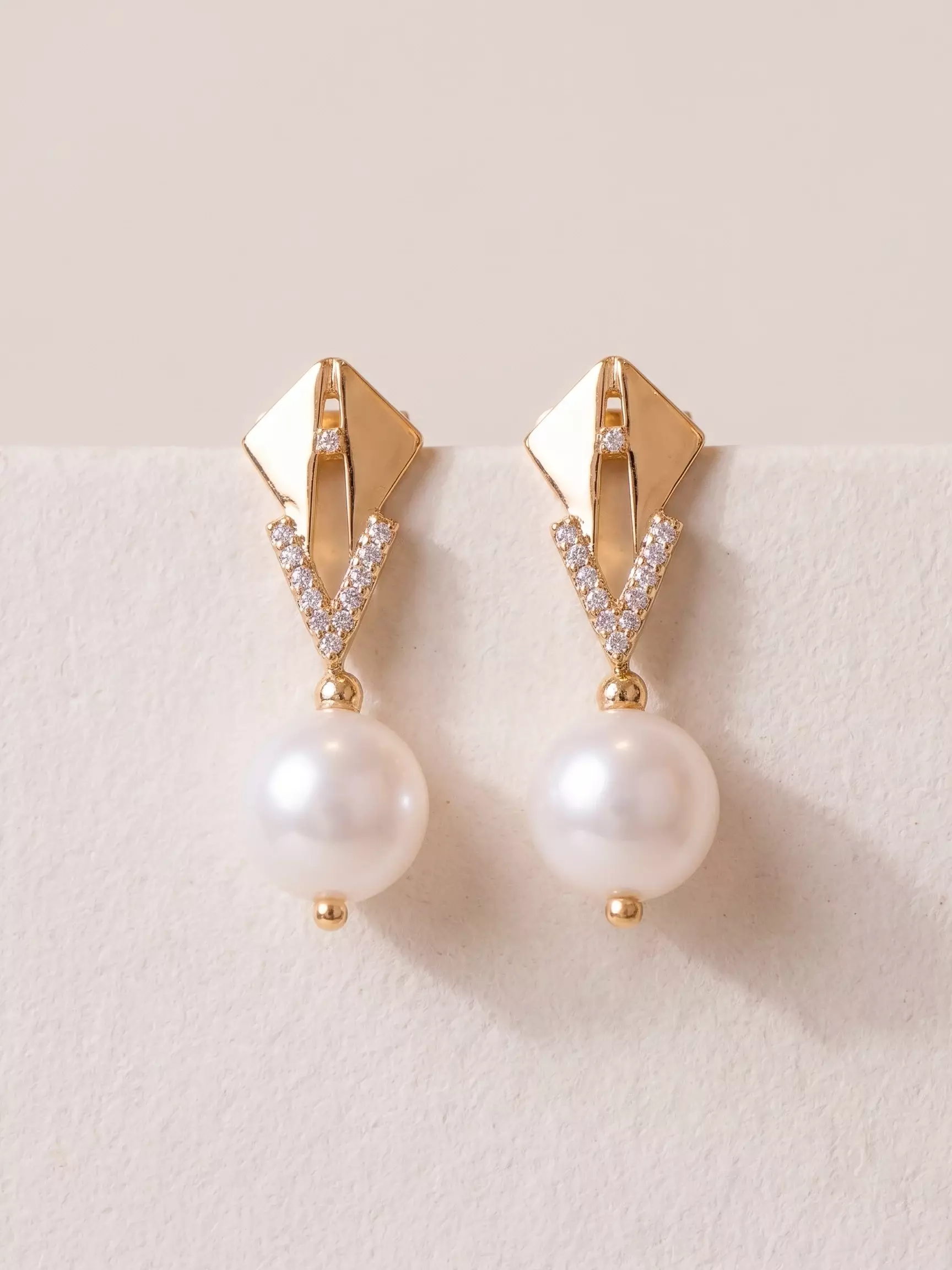 Triangle-base earrings with pavé V and pearl, pair laid down, close-up view