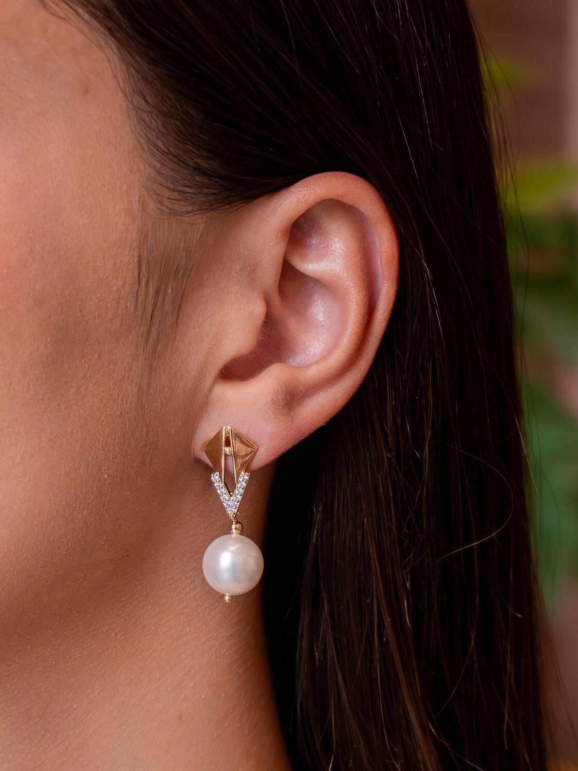 Boucle d’oreille dorée à losange ajouré, V serti de pierres claires et perle ronde pendante.