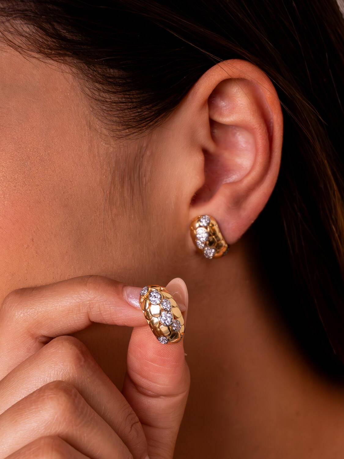 Paire de boucles d’oreilles dorées bombées à relief en écailles et groupes de pierres claires.