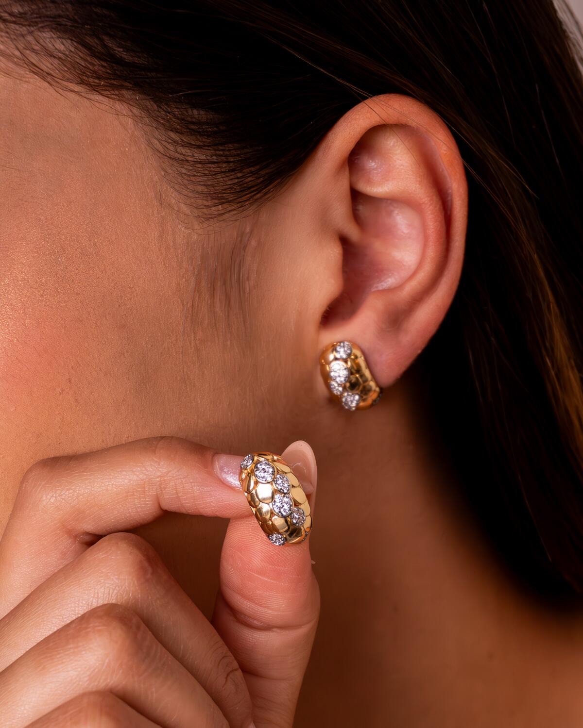 Paire de boucles d’oreilles dorées bombées à relief en écailles et groupes de pierres claires.