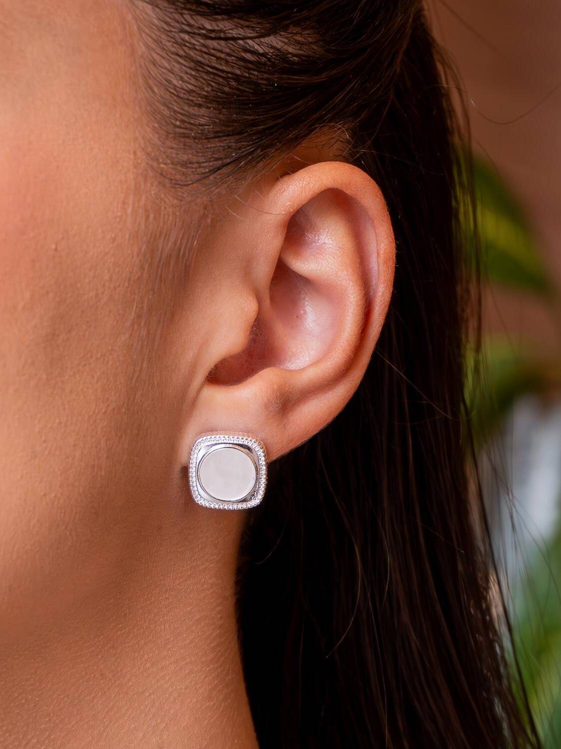 Boucle d’oreille argentée carrée à angles arrondis, liseré scintillant et disque central blanc laiteux.