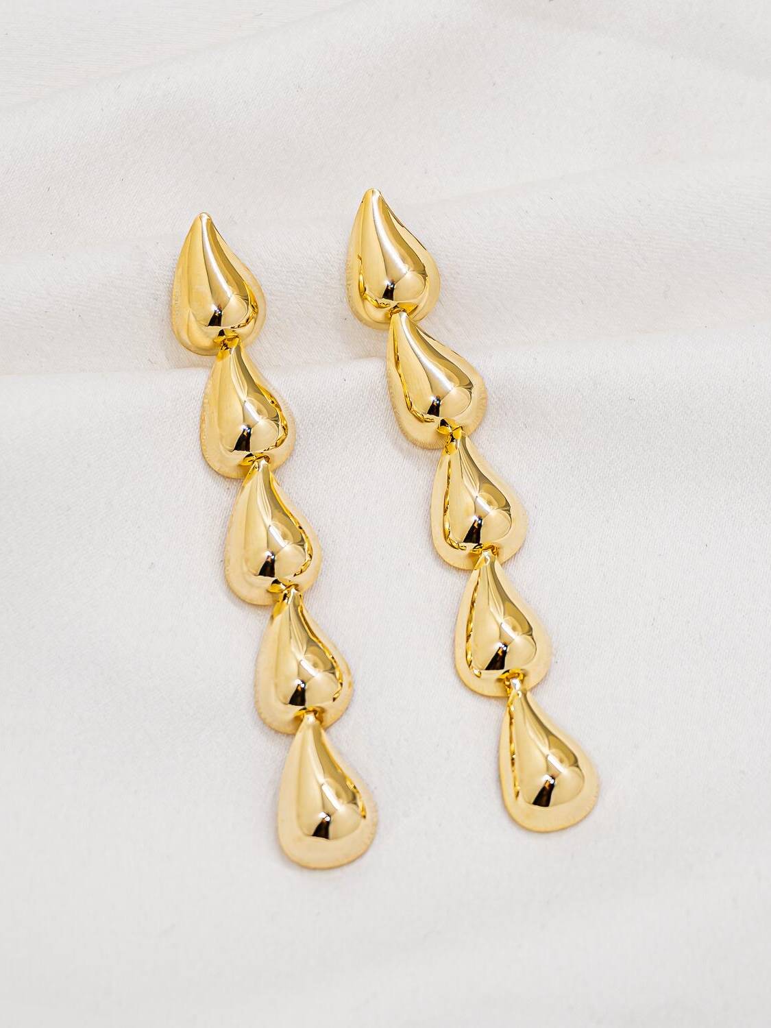 Paire de boucles d’oreilles pendantes dorées formées de cinq gouttes bombées alignées en cascade.
