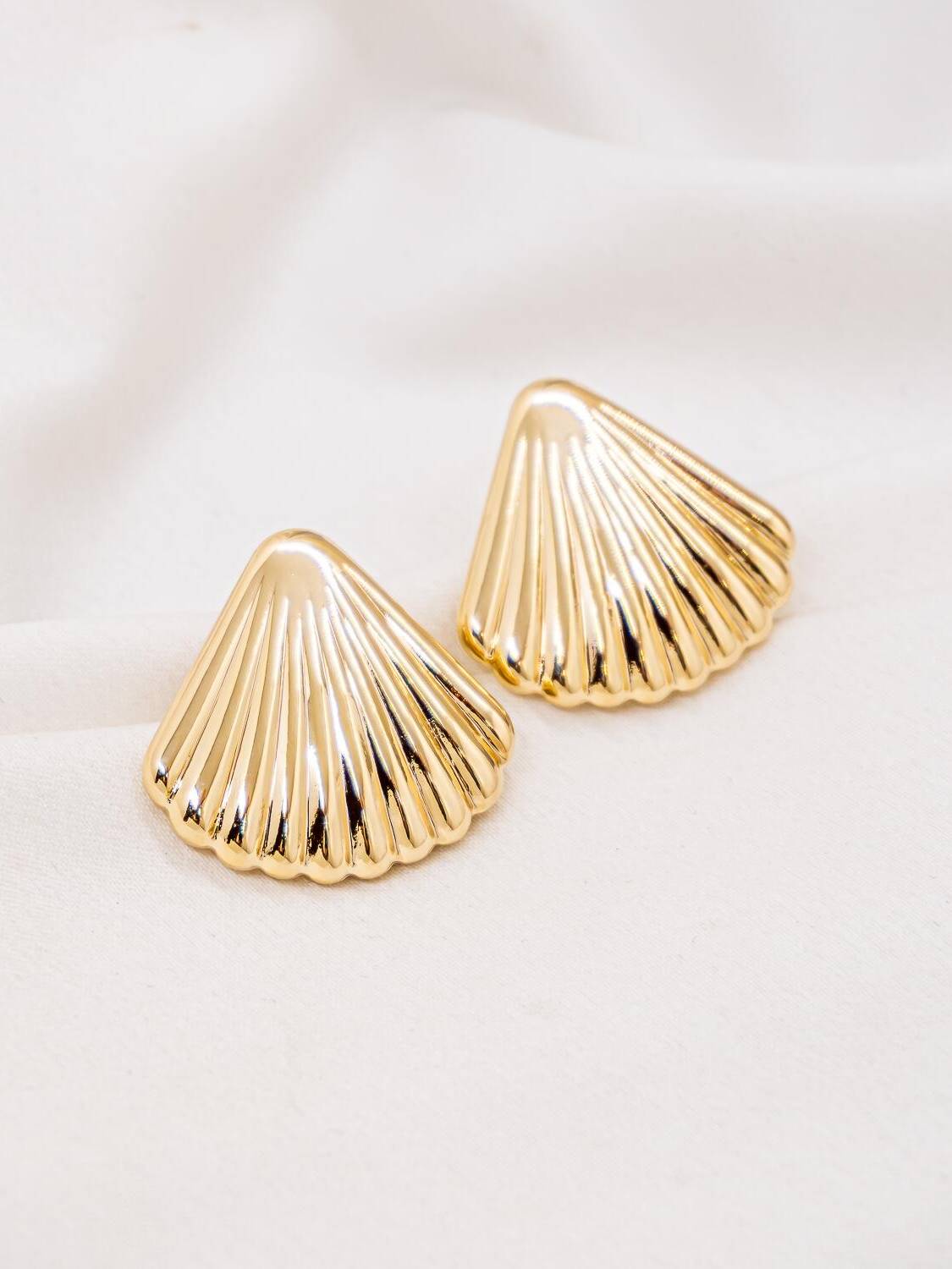 Paire de boucles d’oreilles dorées en forme de coquillage cannelé sur un tissu blanc