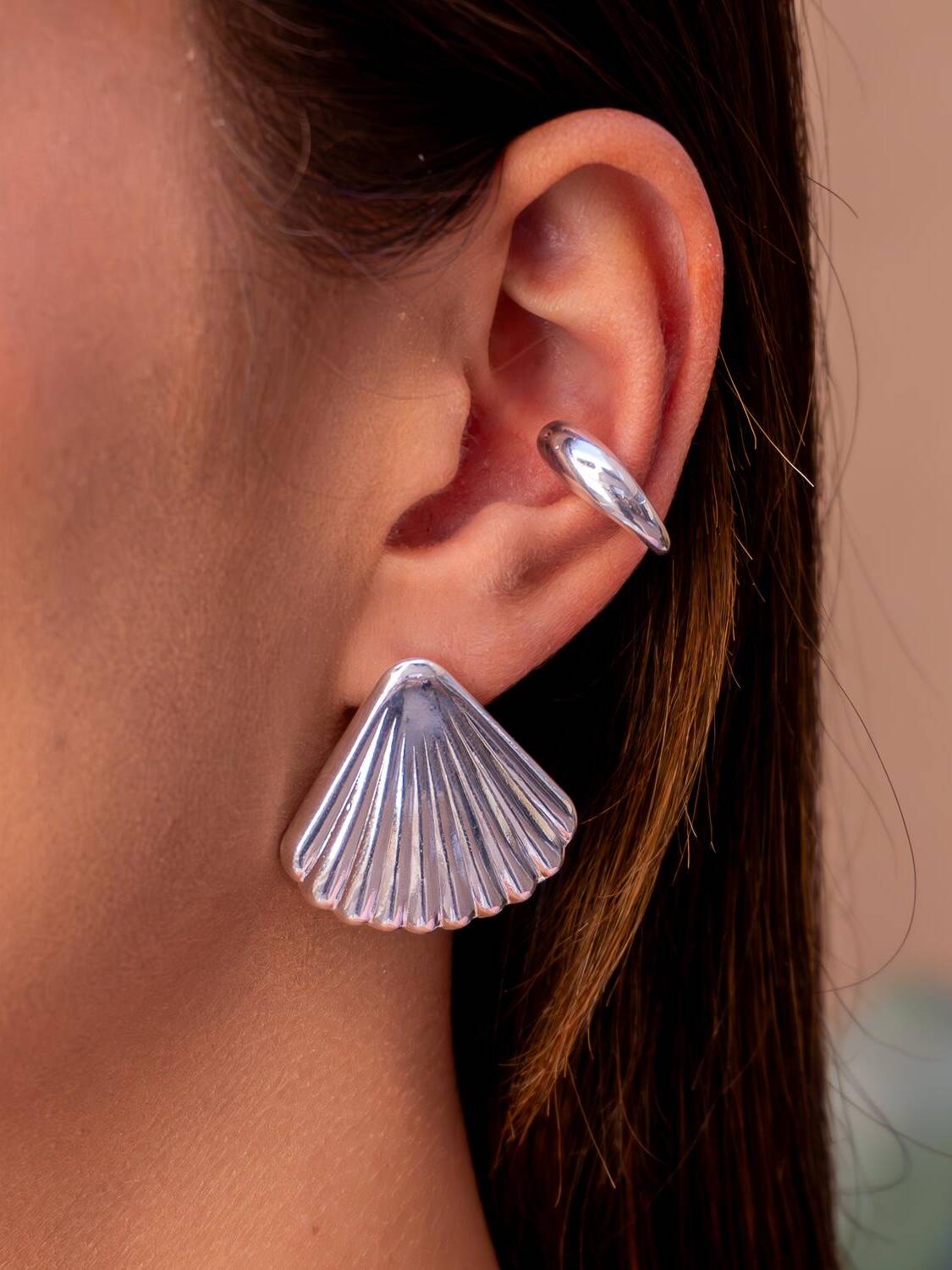 Boucle d’oreille argentée en coquille striée à bord festonné, portée à l’oreille.
