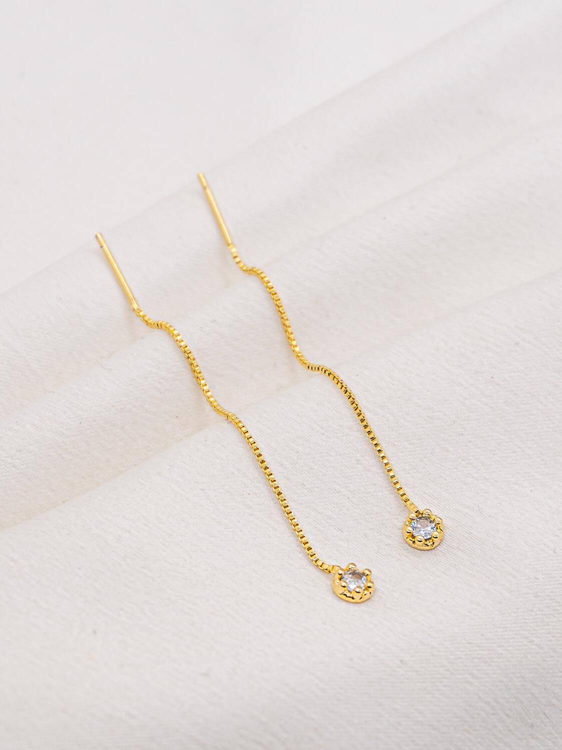 Paire de boucles d’oreilles dorées à chaîne fine terminée par une pierre claire ronde