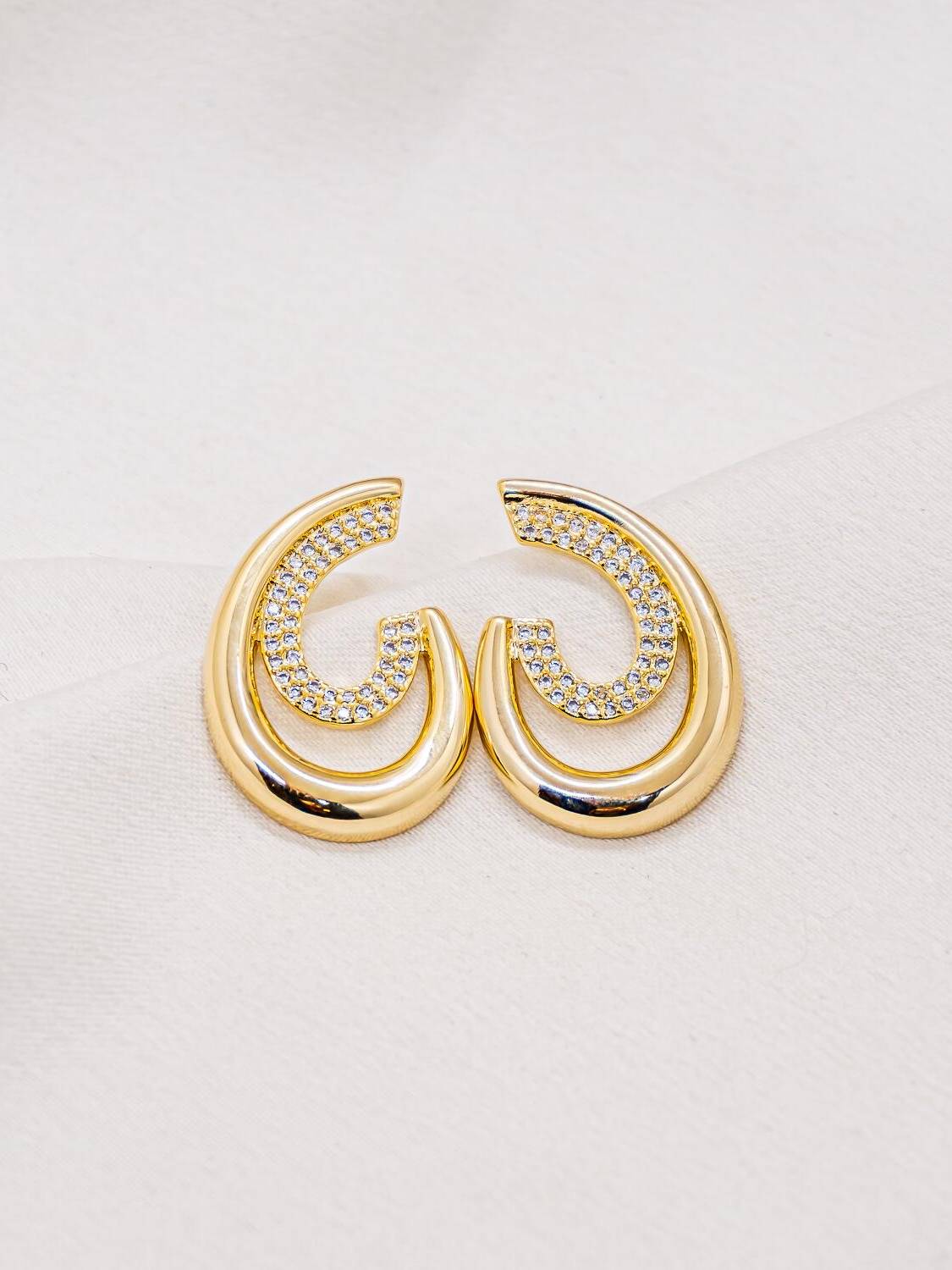 Paire de boucles d’oreilles dorées à double anneau, l’un lisse et l’autre pavé de pierres claires.