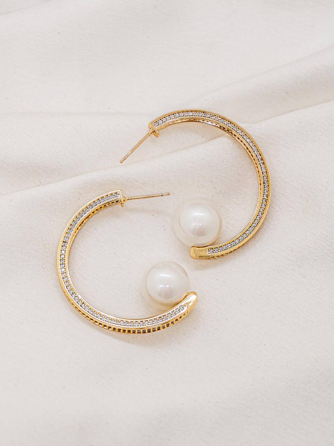 Paire de boucles d’oreilles créoles dorées serties de pierres claires, avec une grosse perle blanche