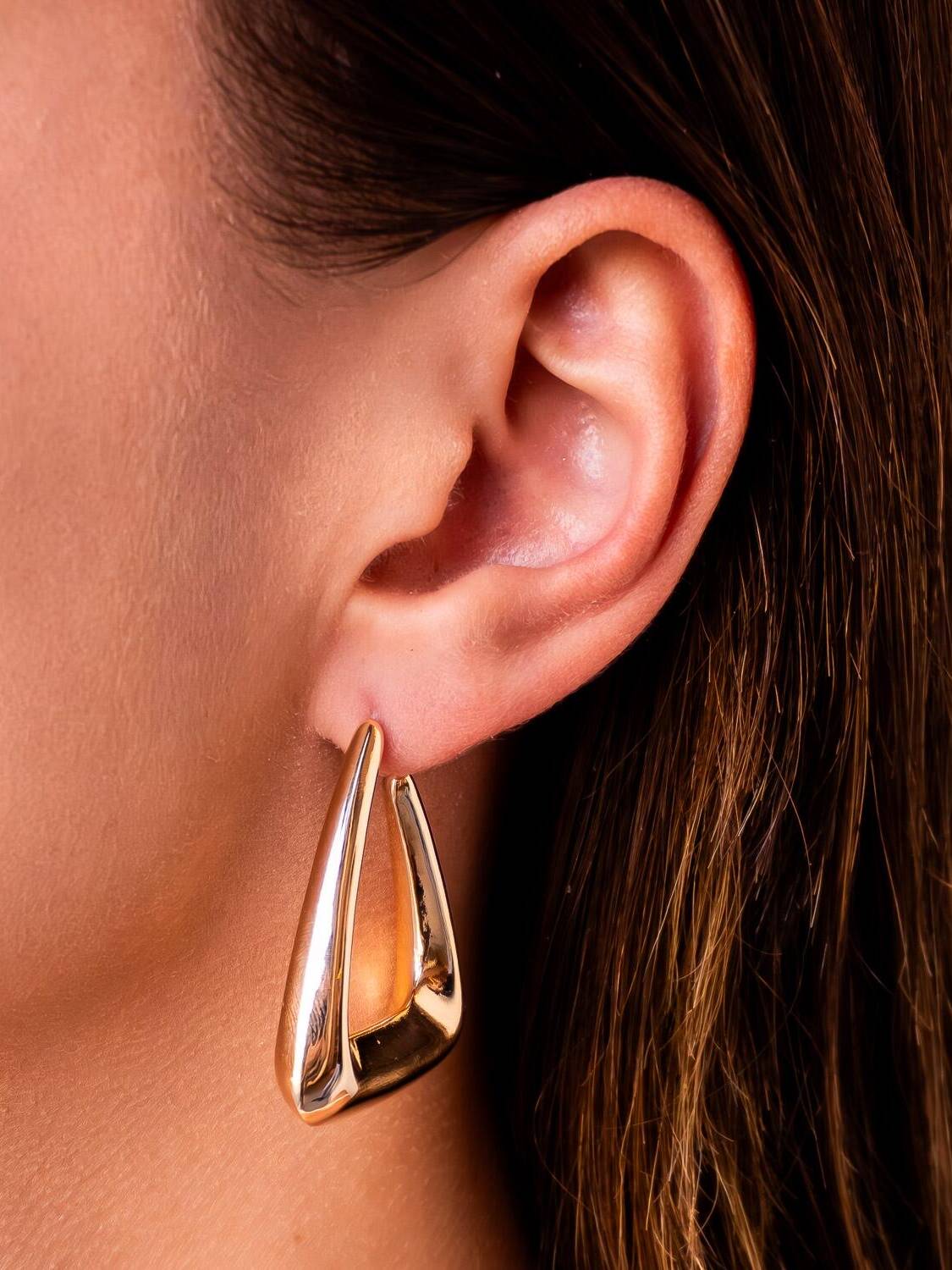 Boucle d’oreille dorée en triangle ajouré aux angles arrondis, métal lisse et brillant.