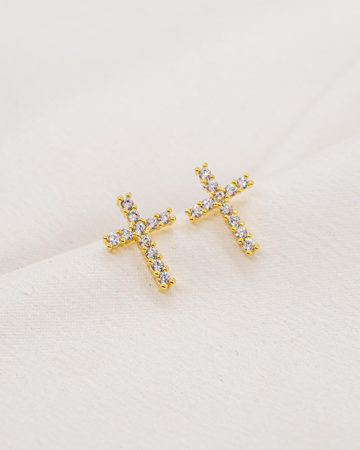 Pair of small gold cross earrings set with clear stones, on white fabric — Product Shot