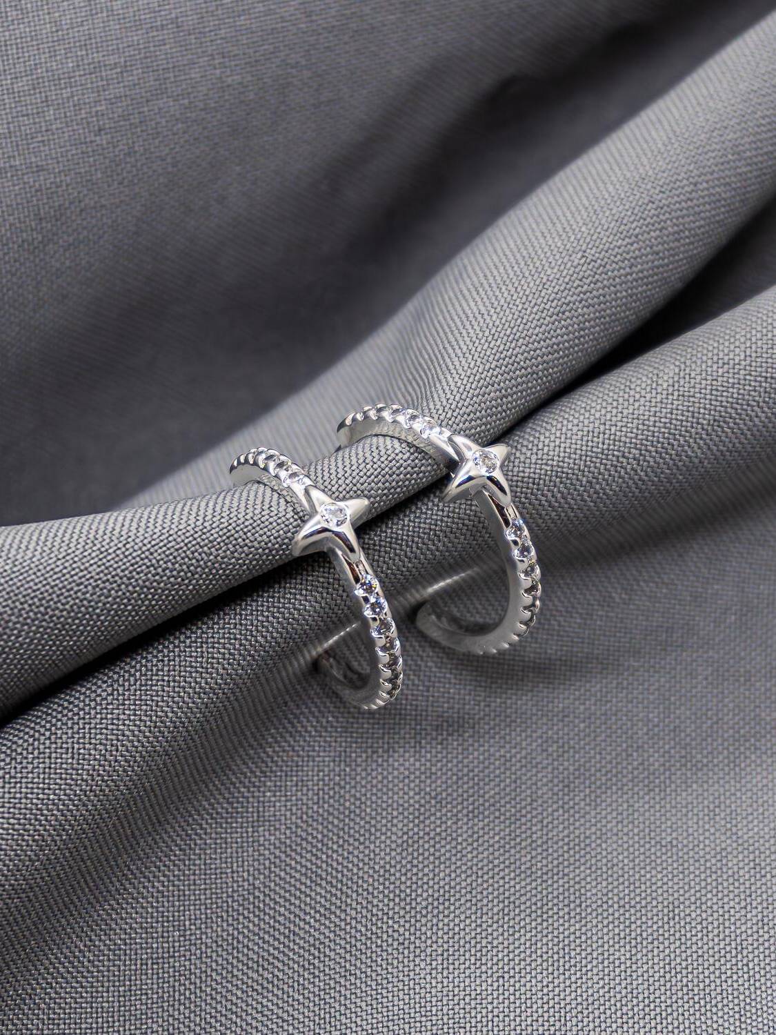 Fines demi-créoles argentées serties de pierres claires, petit motif à quatre branches, sur tissu gris