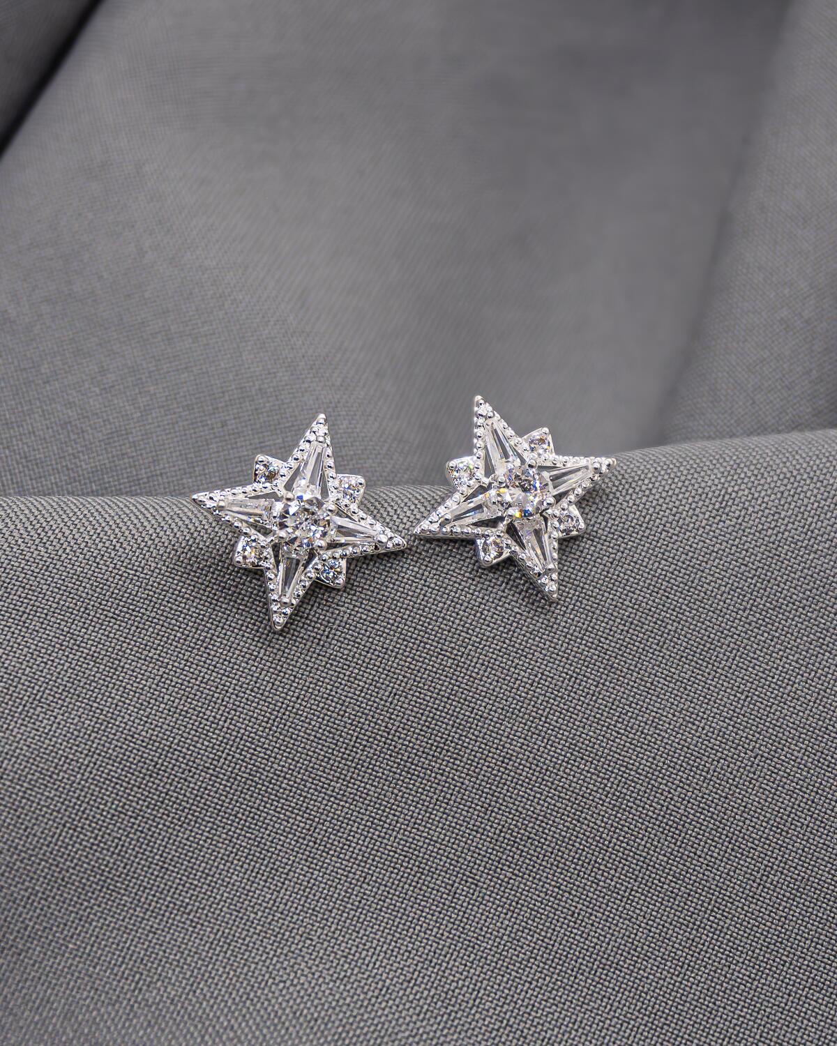 Brincos de estrela prateados com pedras claras sobre tecido cinza