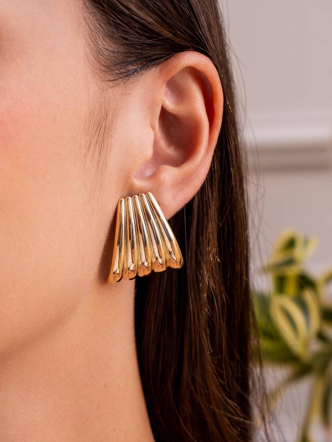 Boucle d’oreille dorée en éventail de lames bombées et polies, portée de profil.