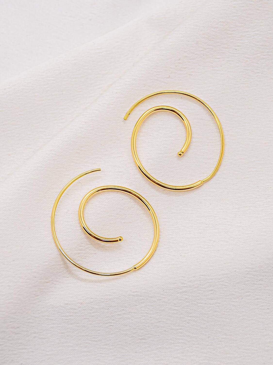 Boucles d’oreilles dorées en fil spirale fin, terminées par une petite boule, sur tissu clair