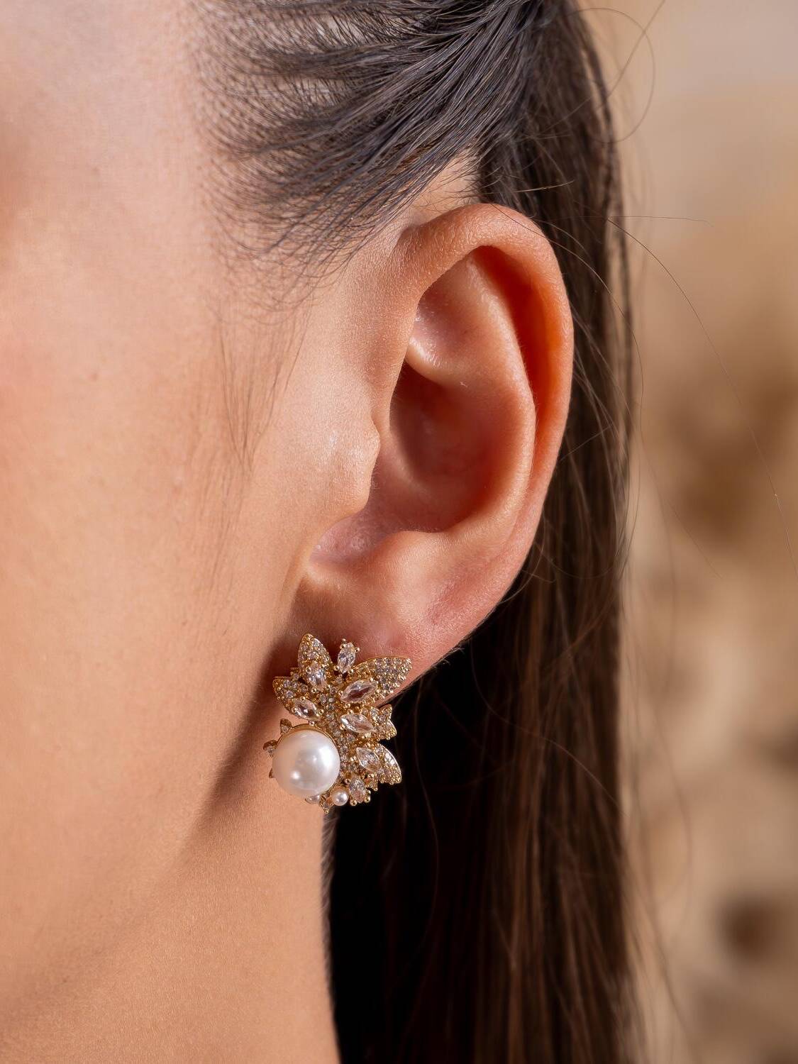 Boucle d’oreille dorée en fleur de pierres claires allongées, avec une perle blanche à la base.