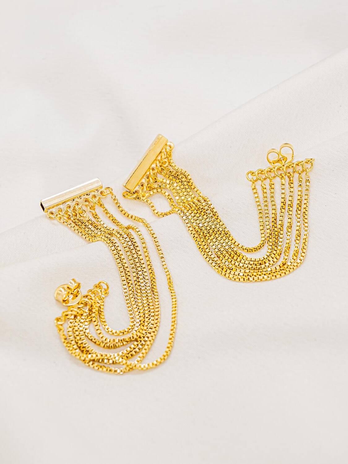 Paire de boucles d’oreilles dorées : une barre fine d’où retombent plusieurs brins de chaîne vénitienne.