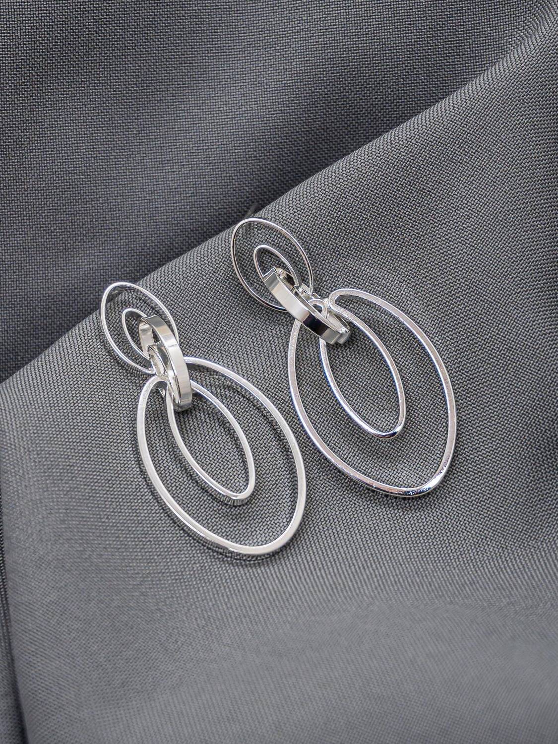 Boucles d’oreilles argentées en ovales ajourés emboîtés, sur un tissu gris foncé