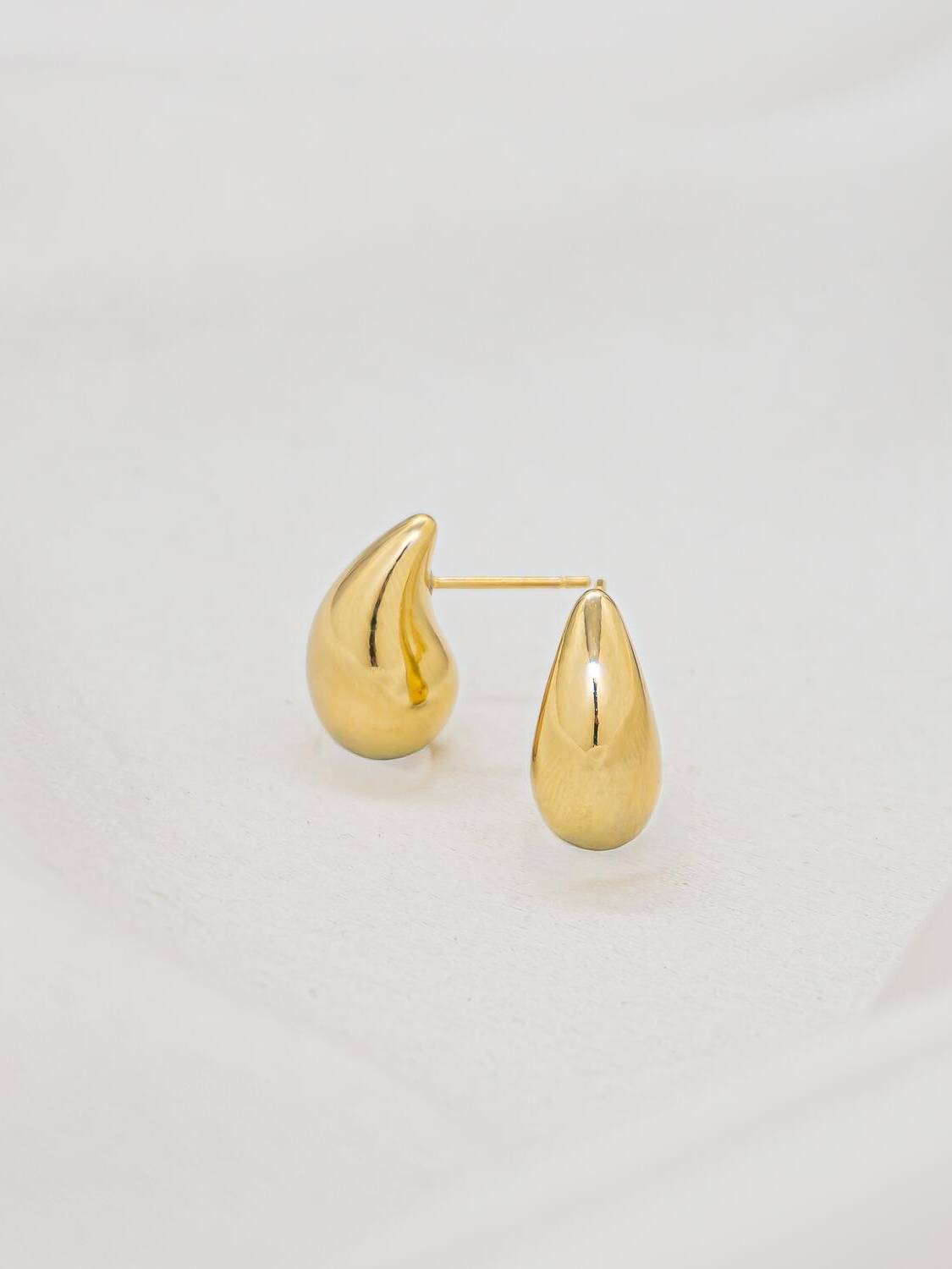 Paire de très petites boucles d’oreilles dorées en goutte lisse, photographiées sur un fond clair.