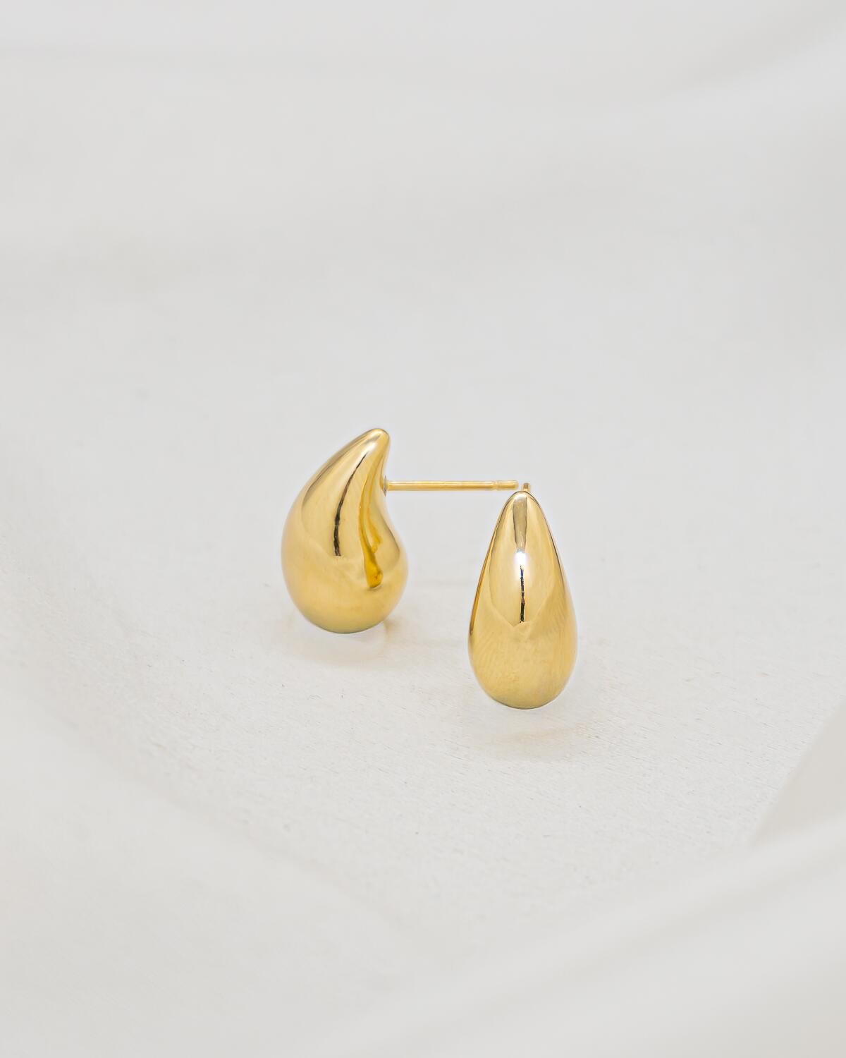 Paire de très petites boucles d’oreilles dorées en goutte lisse, photographiées sur un fond clair.