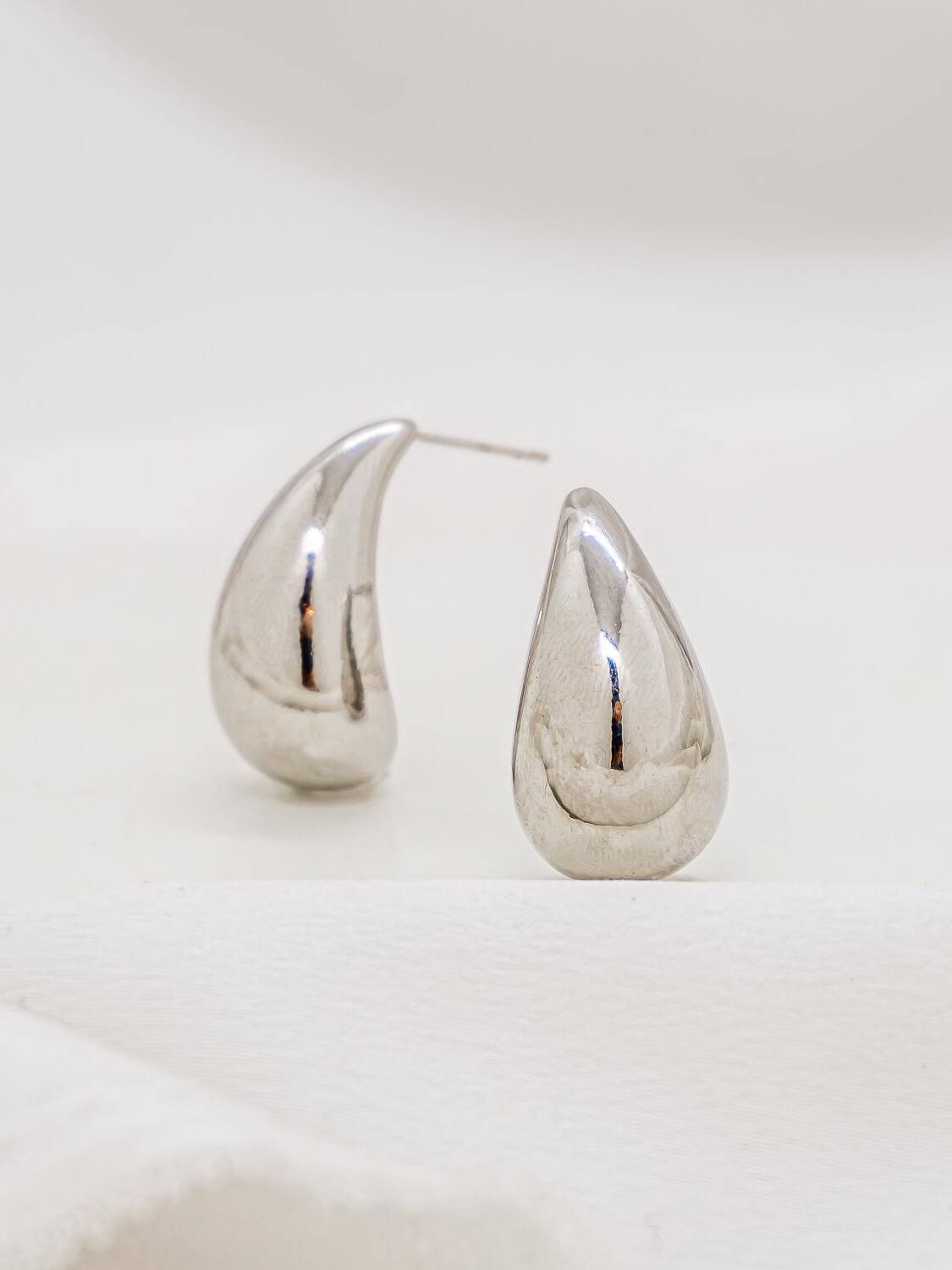 Paire de petites boucles d’oreilles argentées en goutte lisse et bombée, au poli très brillant.