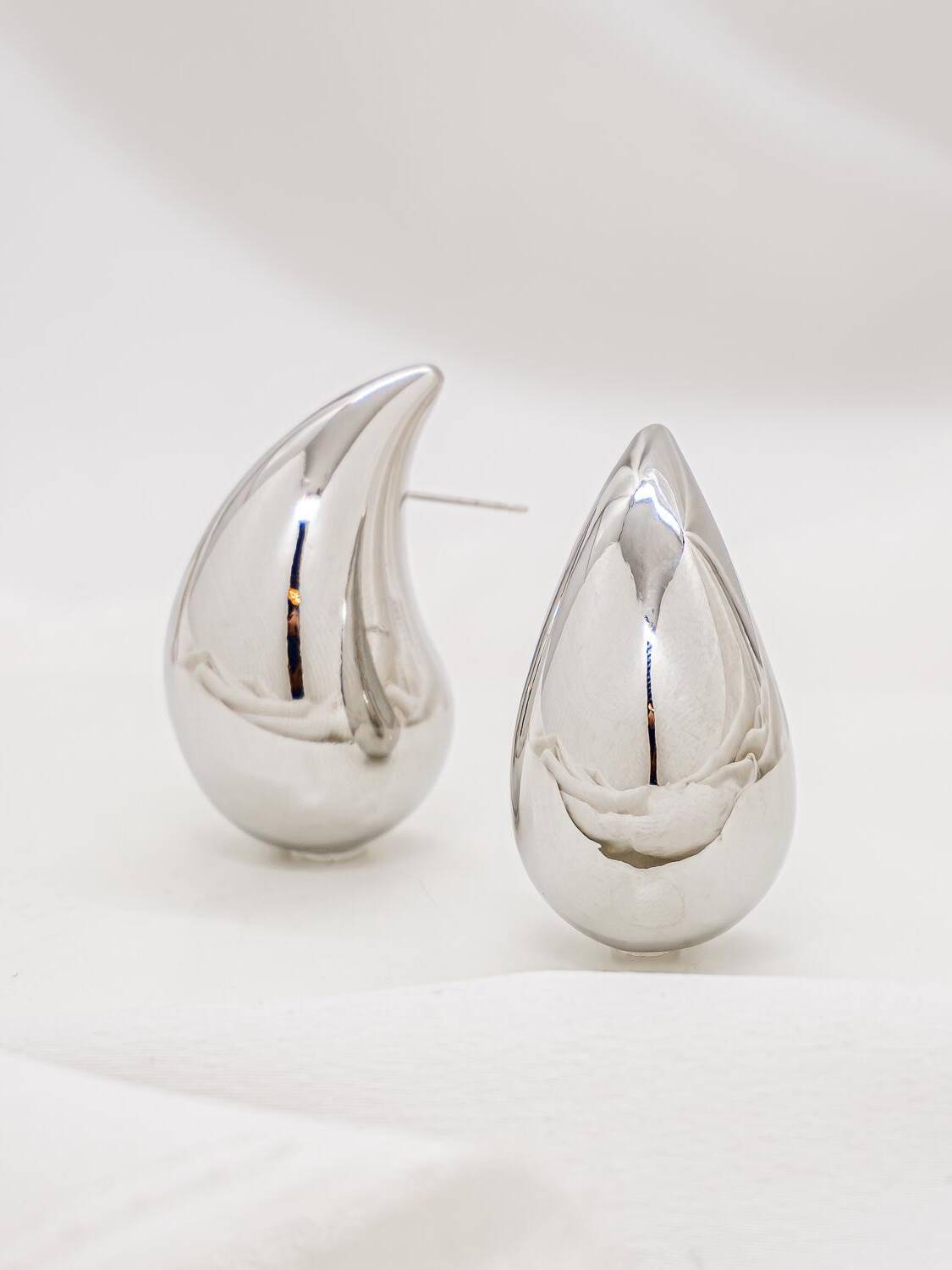 Paire de boucles d’oreilles argentées en goutte bombée, à la surface polie comme un miroir.