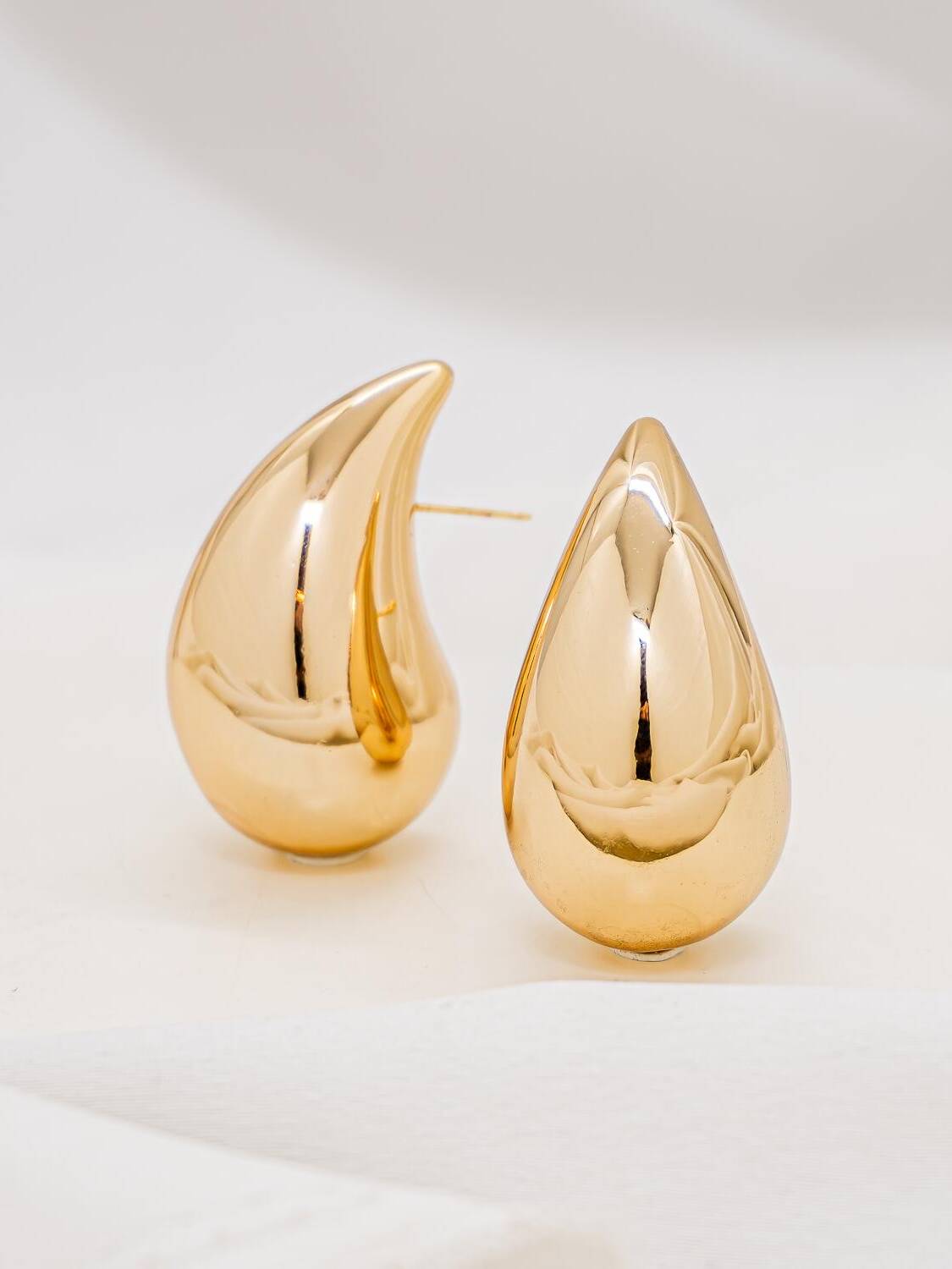 Paire de boucles d’oreilles dorées en goutte bombée et très brillante, vues de trois quarts.