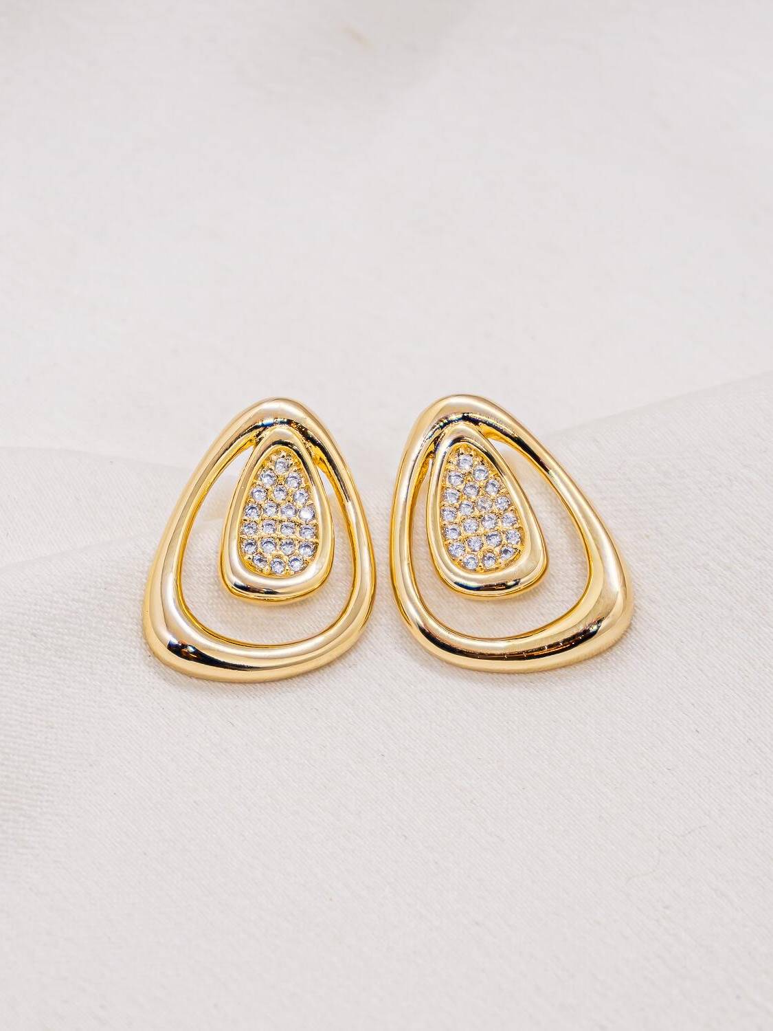 Paire de boucles d’oreilles dorées en goutte ajourée, avec un cœur serti de petites pierres claires.