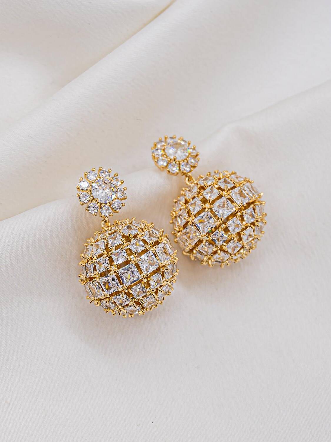 Maxi boucles d’oreilles dorées, boule de pierres claires carrées sous une petite fleur sertie