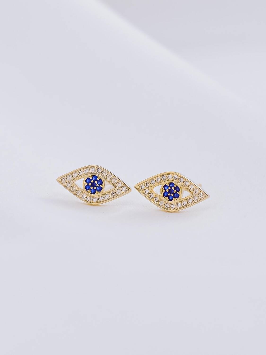 Paire de boucles d’oreilles dorées en forme d’œil grec, pierres claires et centre bleu