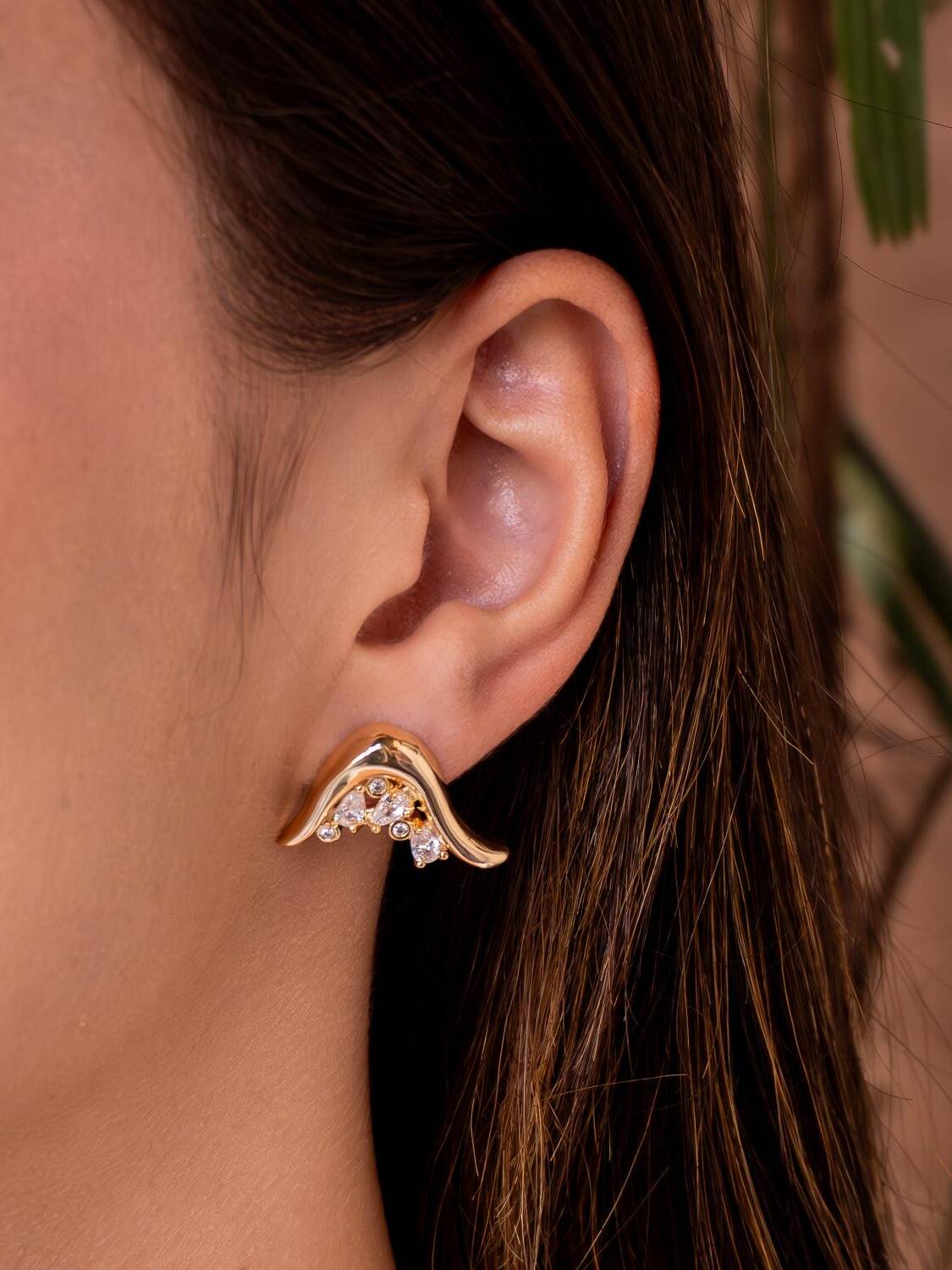 Boucle d’oreille dorée à ligne ondulée lisse et petites pierres claires serties au creux.