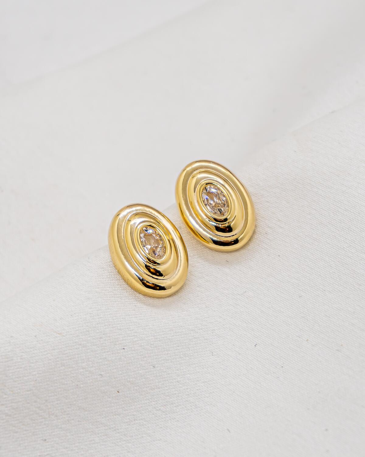Paire de boucles d’oreilles ovales dorées à reliefs concentriques et pierre claire centrale