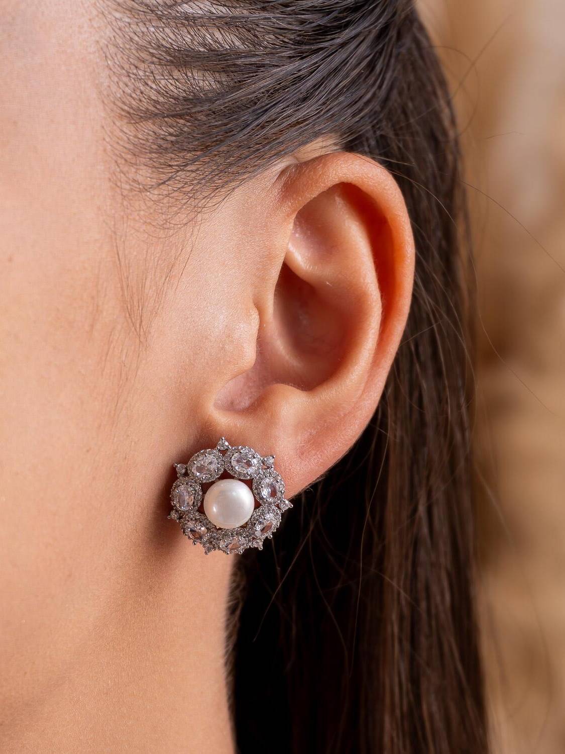 Boucle d’oreille ronde argentée : perle blanche centrale entourée d’une couronne de pierres claires ovales.