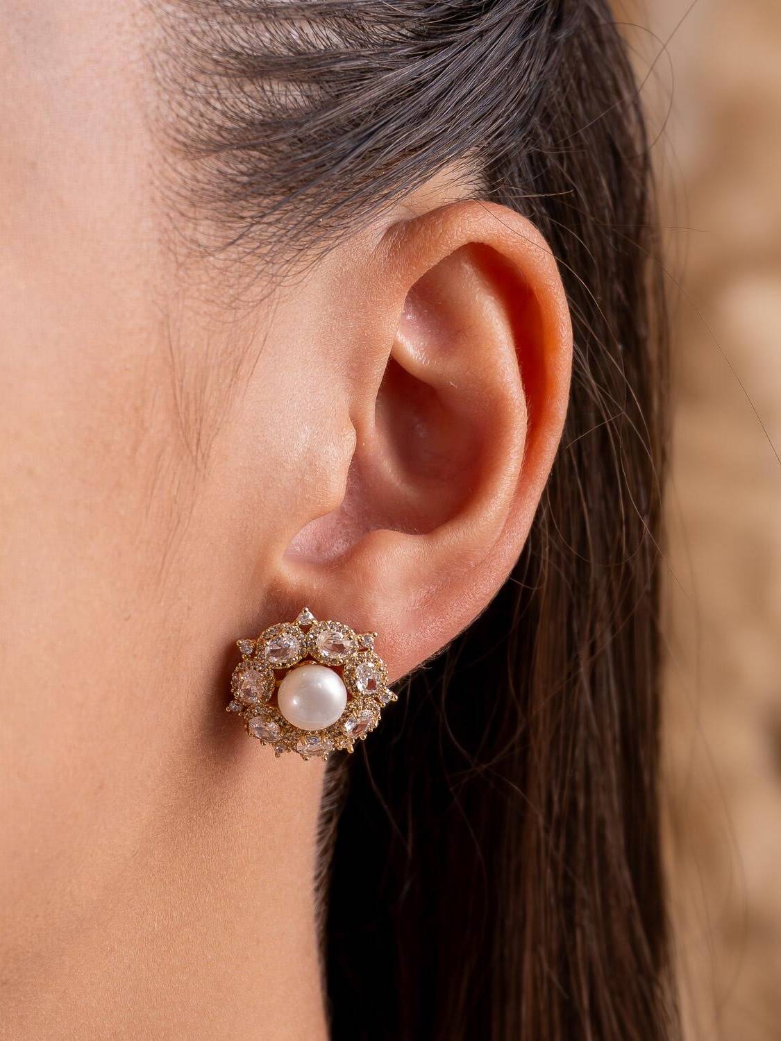 Boucle d’oreille ronde dorée : perle blanche centrale et couronne de pierres claires ovales.