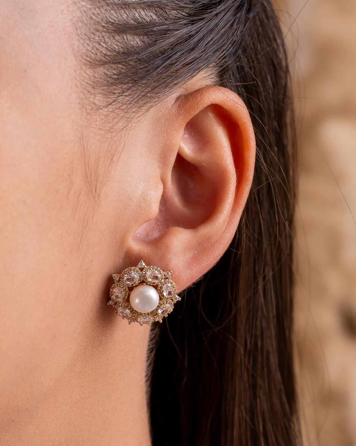 Boucle d’oreille ronde dorée : perle blanche centrale et couronne de pierres claires ovales.