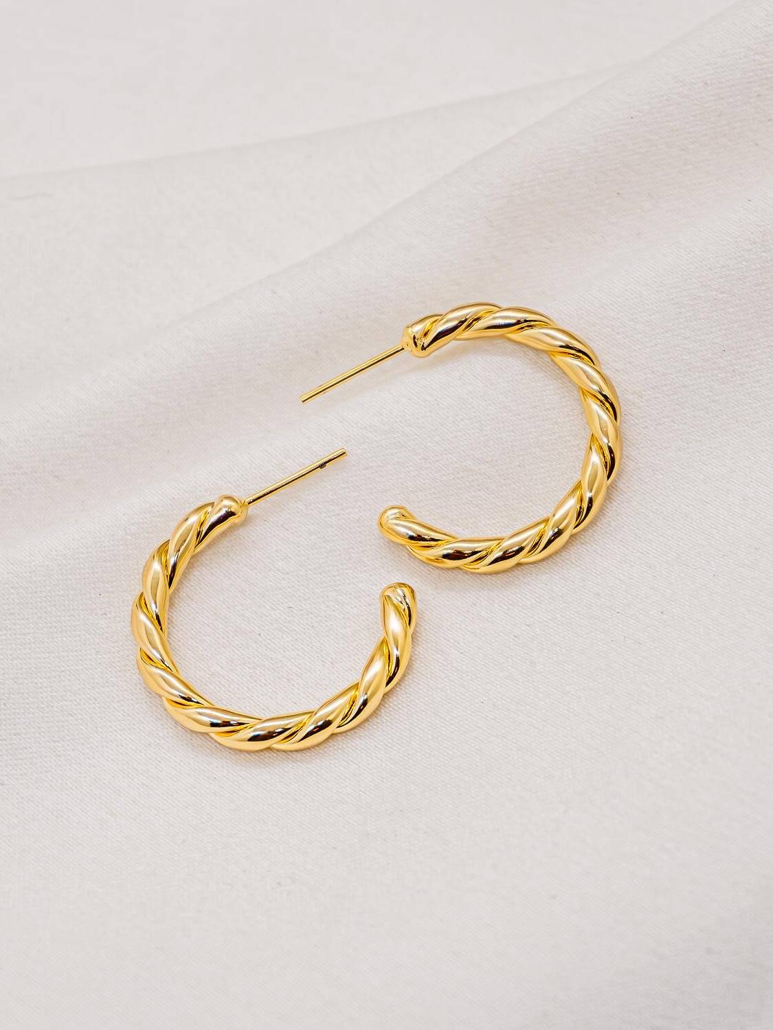 Paire de créoles dorées torsadées, ouvertes, posées sur un tissu clair