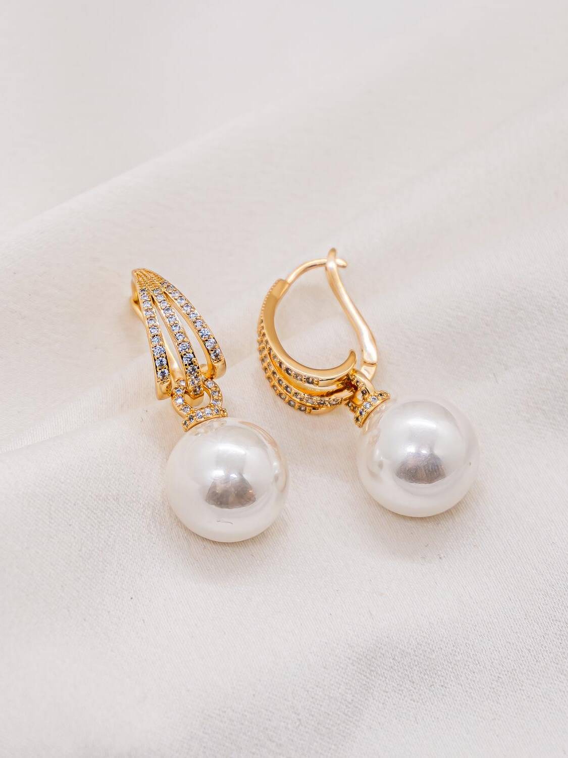 Paire de boucles d’oreilles dorées serties de pierres claires avec une grosse perle blanche pendante