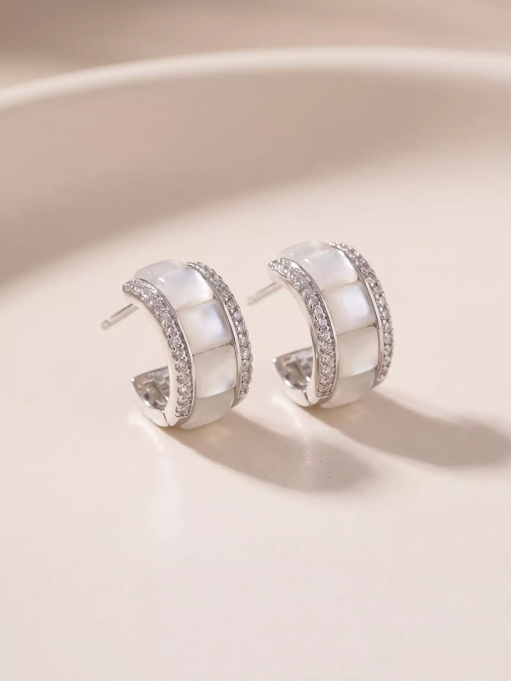 Small mother-of-pearl half-hoop earrings with a set border and silver finish, pair laid flat, close-up view