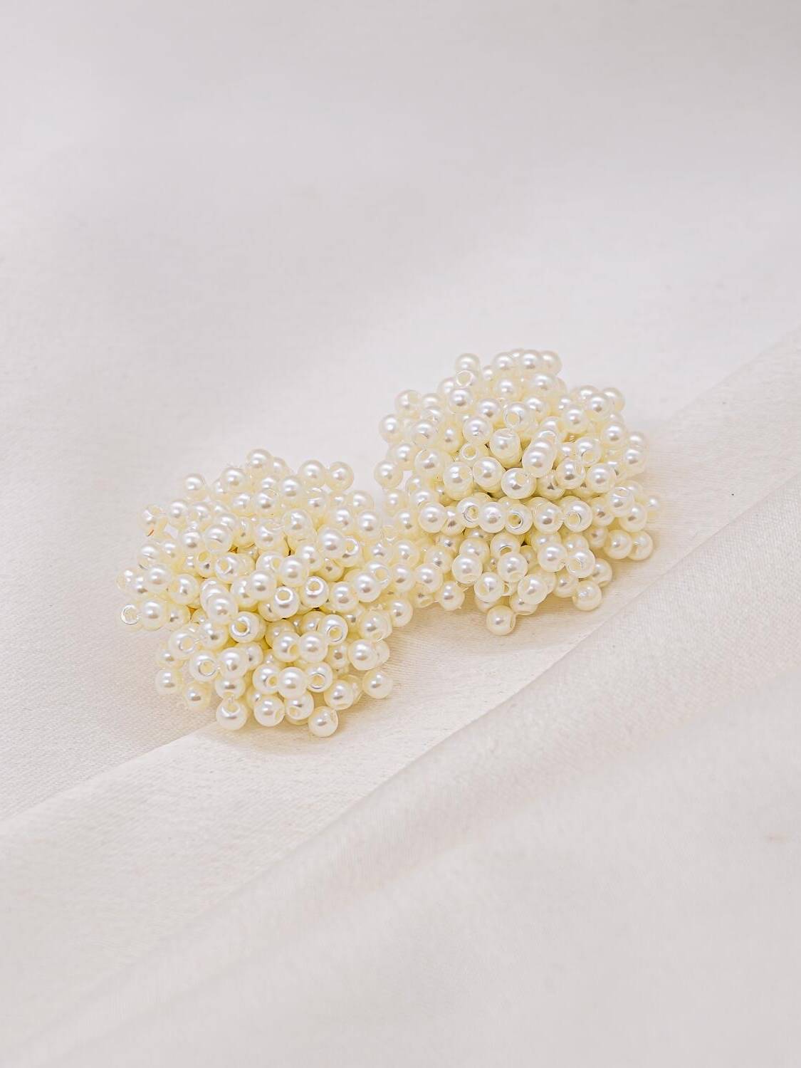 Paire de boucles d’oreilles en grappes de petites perles blanches sur un tissu clair