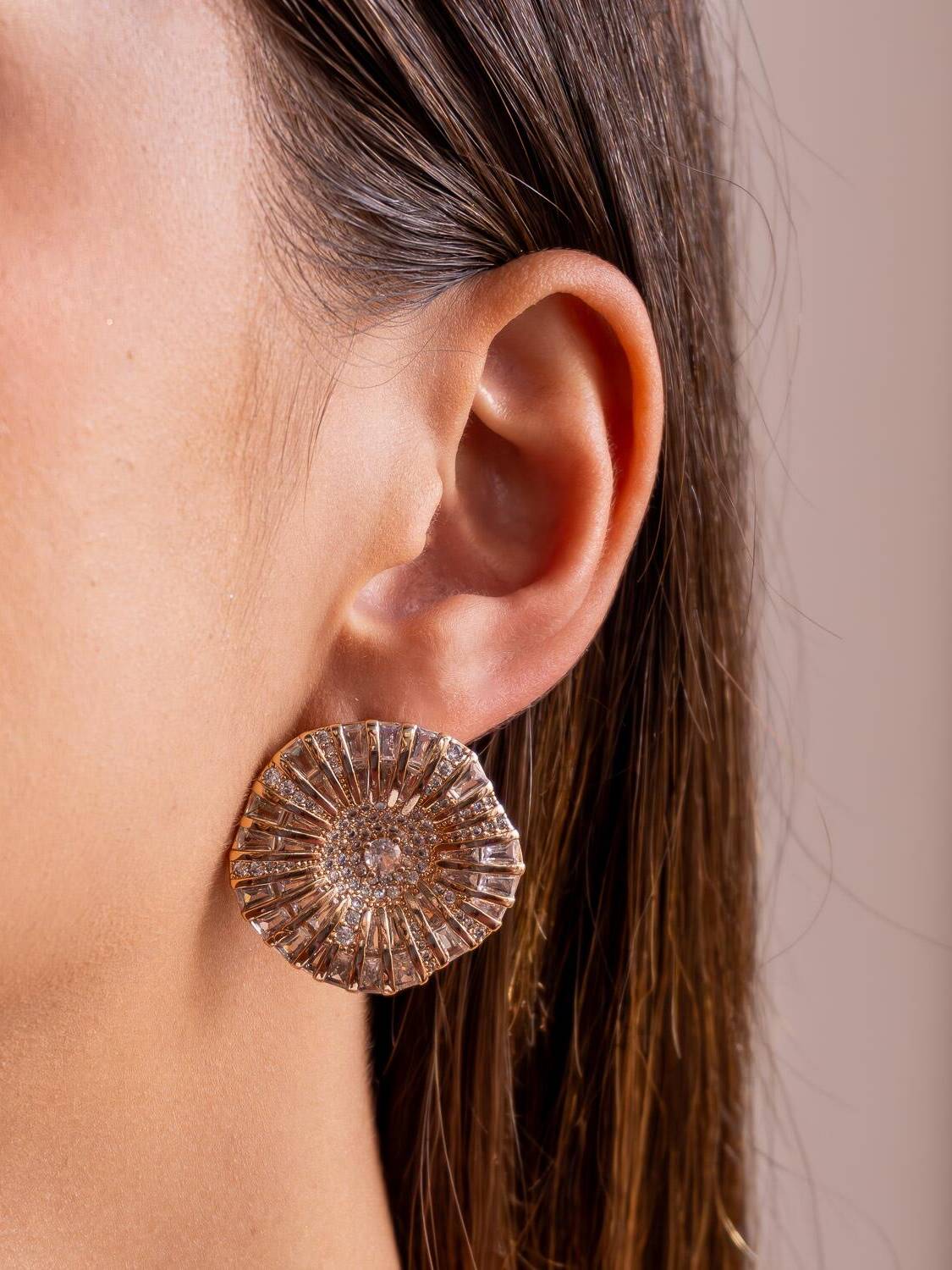 Boucle d’oreille ronde dorée aux bords ondulés, pierres claires rayonnantes autour d’un centre serti.