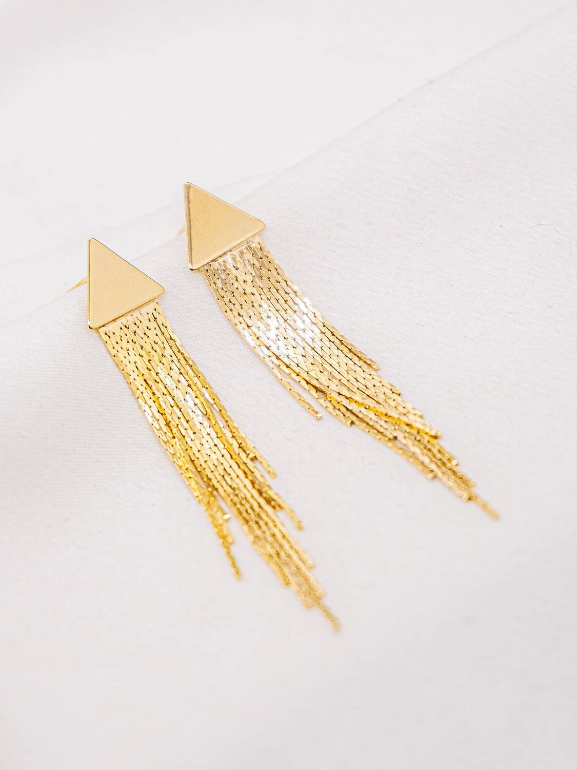 Paire de boucles d’oreilles dorées : triangle lisse prolongé par de fines franges de chaînes.