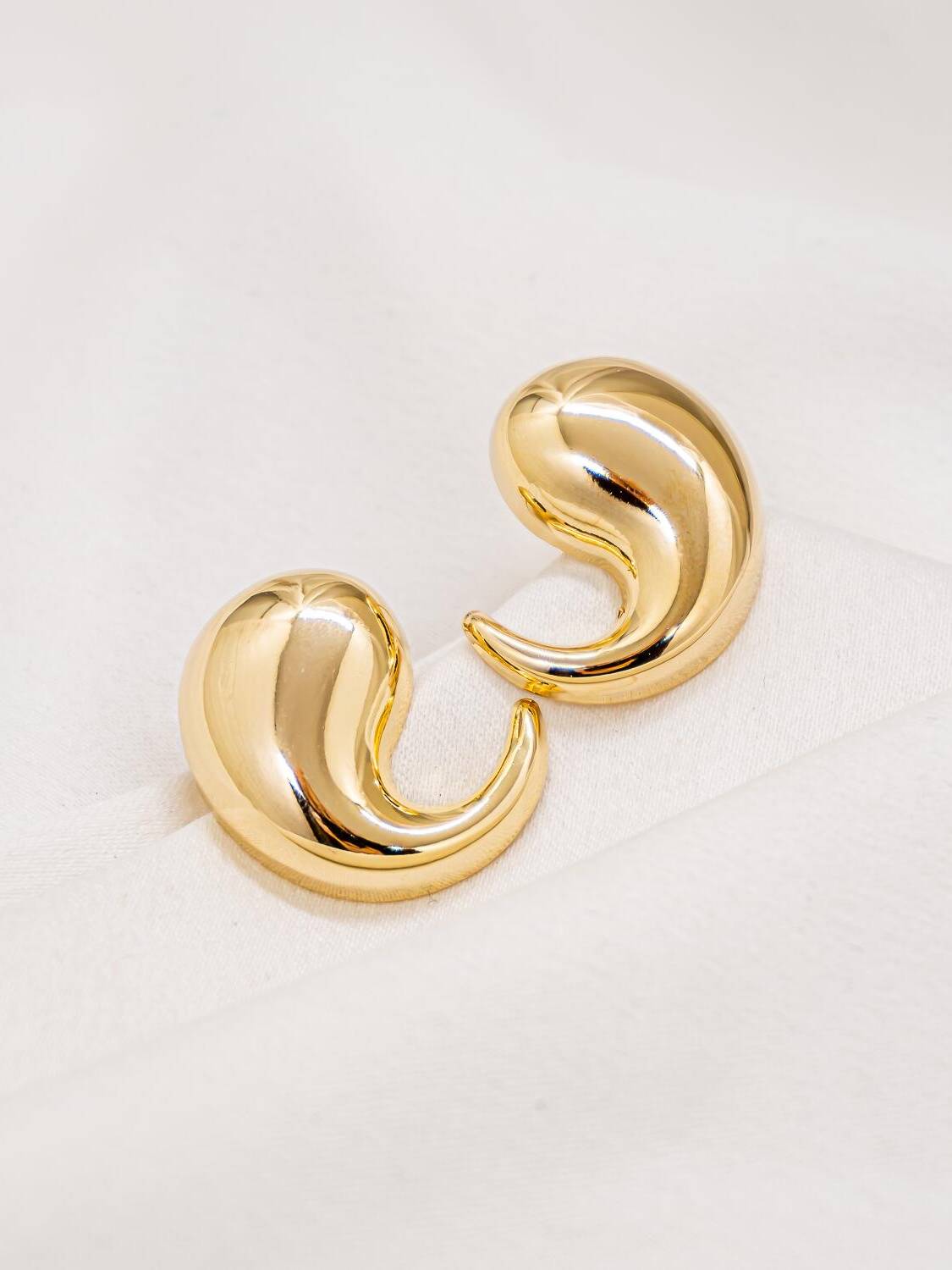 Paire de boucles d’oreilles dorées en forme de virgule bombée, au métal lisse et très brillant.