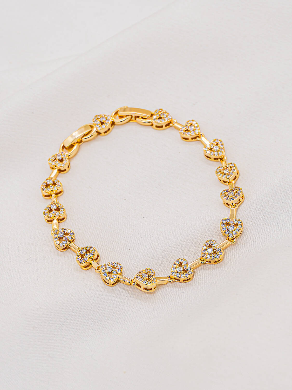 Bracelet doré de petits cœurs sertis de pierres claires reliés par de courts maillons