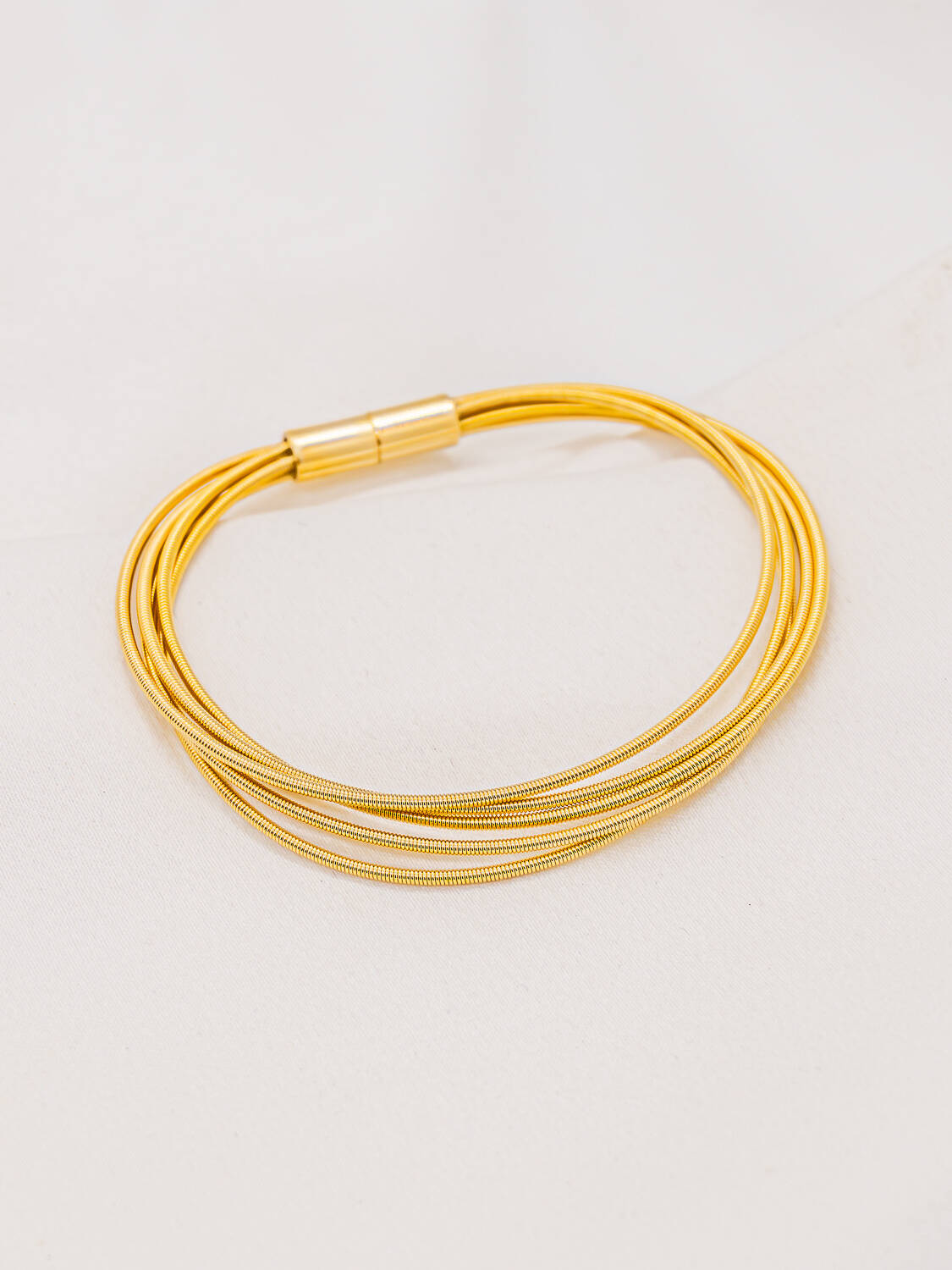 Bracelet doré de fils fins superposés à fermoir cylindrique, posé sur un tissu clair